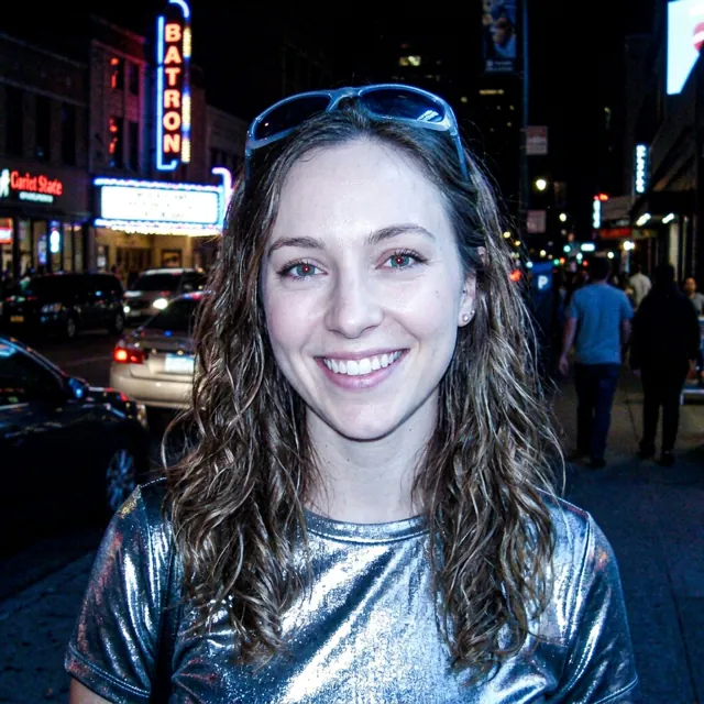 A flash photo of the woman in a silver top on a city street at night